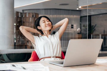 Eastern businesswoman with closed eyes professional employee feeling relaxation at work doing stretching exercises. Smiling asian woman making break, working stress relief on laptop computer in office