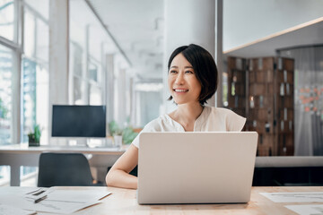 Professional female executive entrepreneur in suit working on computer pc at company workplace, looking dreaming. Asian smiling middle aged business woman using laptop at work in office. Copy space
