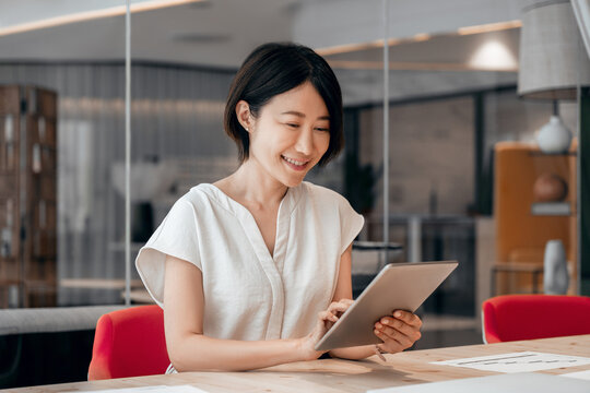 Smiling ceo entrepreneur businesswoman leader using touchsceen pc device in office. Asian middle-aged woman using tablet reading news browsing, doing online work, business learning or communication