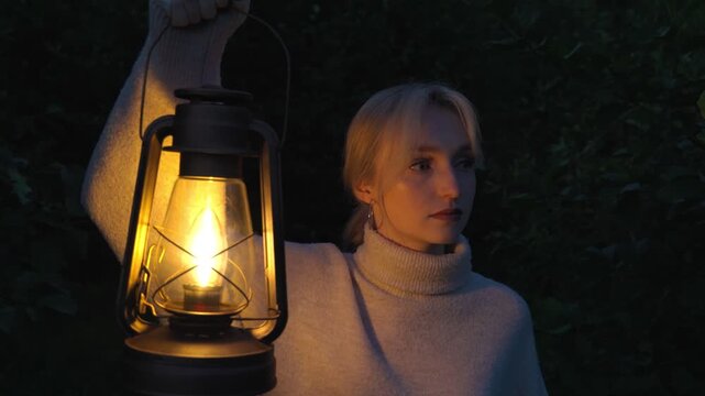 A lonely, anxious woman walks through the forest at night with a burning kerosene lamp in her hand. The concept of anxiety, arousal and fear.