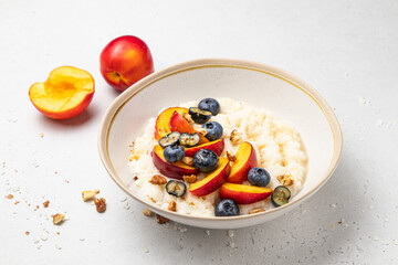 Rice porridge or pudding with milk, blueberries, nectarines, walnuts and honey in a bowl on the table. Rice cereal healthy breakfast. Home cooking. Selective focus.