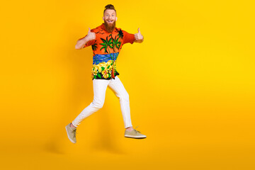 Fototapeta premium Energetic Young Man Wearing Tropical Shirt and White Pants Posing on Bright Yellow Background While Giving Thumbs Up
