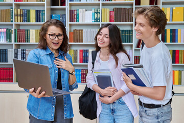 Two teenage students meeting talking with female teacher in library