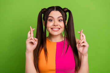 Portrait of a cheerful young woman with twin ponytails crossing fingers against a green background