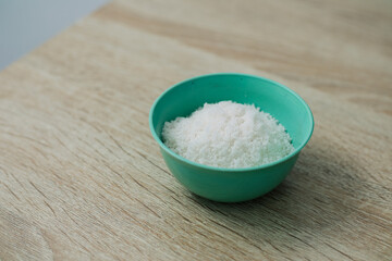 A close up of white crystalized powder in a light green bowl on a wooden surface, food preparation concept