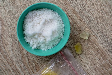 Close-up of potentially illicit substances including a crystal-like material in a blue bowl and plastic bag on a table