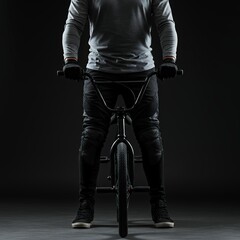 Obraz premium BMX bike rider in protective gear and casual dark clothing on black freestyle bicycle in dramatic moody studio lighting with gradient gray background