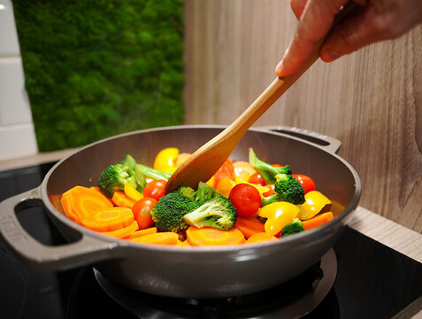 Hand stirring colorful vegetables in a pan on stovetop