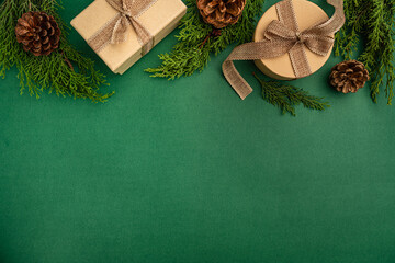 Natural holiday flat lay with kraft-wrapped gifts, pine cones, greenery, and wooden snowflakes on a green background.