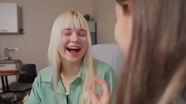 Close up of cheerful blonde girl with open mouth laughing as she successfully catches last popcorn thrown by friend during fun indoor moment
