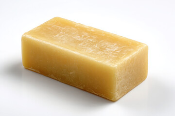 Close up of a rectangular bar of yellowish soap sitting on a plain white surface with soft shadows
