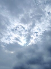 Cloudy sky during the day, with a sun hidden by the clouds shining brightly