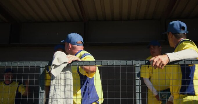 Reacting as play intensifies Diverse male baseball teammates gesturing in dugout with fence, gloves