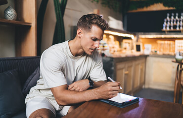 Fototapeta premium Freelancer drawing with stylus on tablet at café-style table, portraying deep creative focus, mobile work habits, and integration of digital tools into everyday professional life.