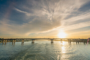 Naklejka premium Stunning sunset view of a bridge over the Nile River near Temple of Luxor in Egypt, with golden reflections on water and a colorful sky.