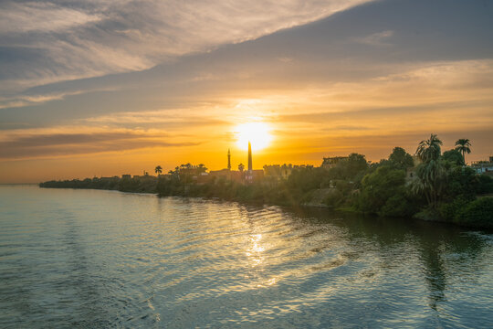 Warm sunset light reflects on the Nile River near Esna Lock, Egypt, with a minaret and palm trees lining the riverbank.