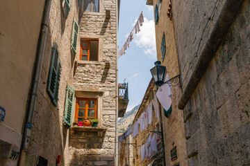 charming narrow alley in kotor, montenegro with historic stone buildings, colorful windows, hanging laundry, and a vintage lantern under a clear blue sky