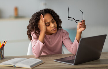 Tired student. African american schoolgirl studying online on laptop at home. Teen female student exhausted from looking at screen, doing assignments or communicating on web