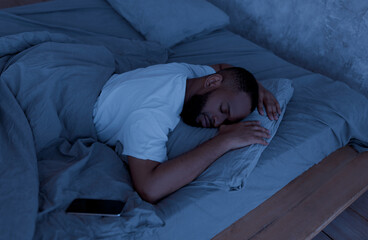 African American Man Sleeping, Resting In Bed In The Night At Home, Lying Near Smartphone. Always In Touch, Busy And Stressed Modern Life, Mobile Phone And Gadget Addiction Concept