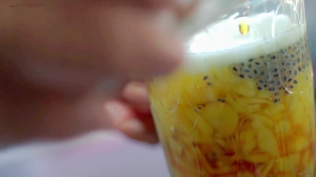 Close-up of yellow cendol dessert in a glass with basil seeds and coconut milk, perfect for tropical drink, summer refreshment, and authentic Southeast Asian beverage concepts.