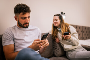 Young couple in hotel room, girlfriend peeking at boyfriend’s phone