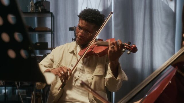 String duo playing musical instruments in studio, young African American man playing violin with focus flowing to girl playing cello