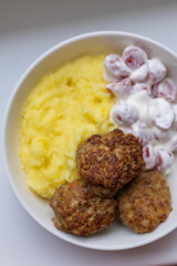 Minced meat cutlets with mashed potato and cherry tomatoes salad with sour creme on white bowl over white background. Top view, flat lay.