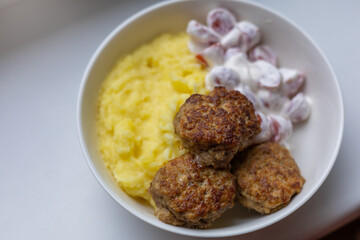 Minced meat cutlets with mashed potato and cherry tomatoes salad with sour creme on white bowl over white background. Top view, flat lay.