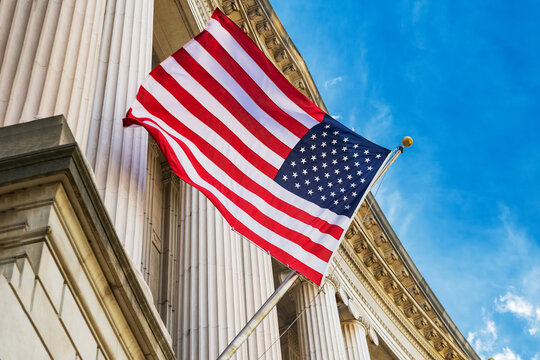 Close-up of American flag on federal building in Washington DC with marble columns, blue sky, and national symbol of independence and freedom.