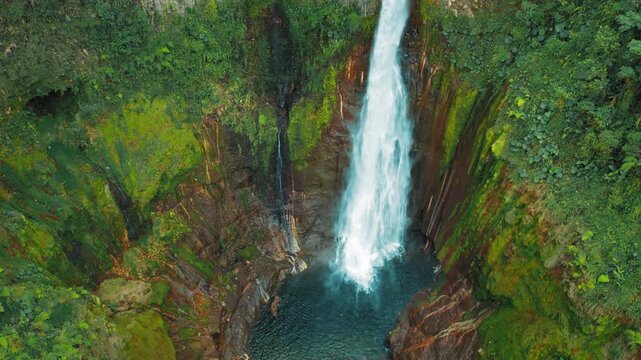 Blue Falls waterfall Catarata del Toro crashing into blue basin surrounded by jungle cliffs in Costa Rica