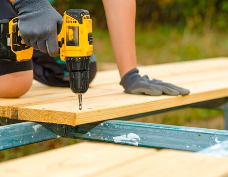 Person Using Yellow Power Drill on Wooden Plank Outdoors in Daylight