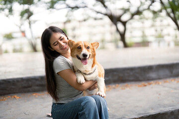 Happy moments. Woman cuddling her corgi dog on park steps.