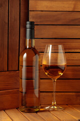 Bottle and glass of white wine on a wooden background.
