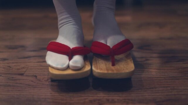 A woman putting on traditional Japanese shoes, such as geta or zori, captured in a close-up moment. The image highlights cultural detail and graceful movement, with attention to traditional attire and