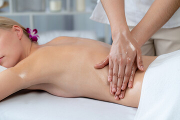 Naklejka premium Caucasian woman customer enjoying relaxing anti-stress spa massage and pampering with beauty skin recreation leisure in day light ambient salon spa at luxury resort or hotel. Quiescent
