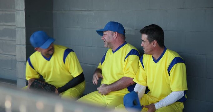 Laughing after shared joke, male baseball teammates passing cap and comforting teammate in dugout