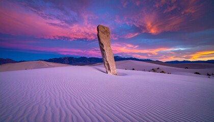 Obraz premium Majestic Stone Slab Stands Tall in Serene White Sand Dunes Under a Breathtaking Sunset Sky, Creating a Dramatic Desert Landscape Vista.