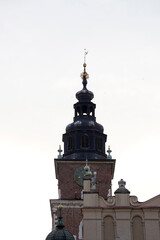 Obraz premium A tall brick clock tower with dark domed spire and golden ornaments rises above ornate facades, symbolizing timeless architecture and the silent passage of centuries.