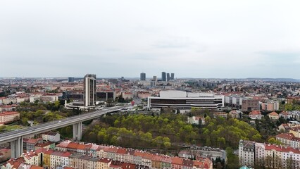Drone view of a modern highway bridge crossing historic city rooftops. Urban contrast of red-tiled houses, tall towers, and green park below. Vibrant cityscape stretching to the horizon.