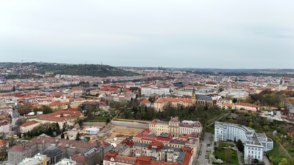 Aerial panorama of a historic European city with endless red rooftops, domed churches, and a modern tower rising above. Contrast of heritage architecture and urban development in one frame.