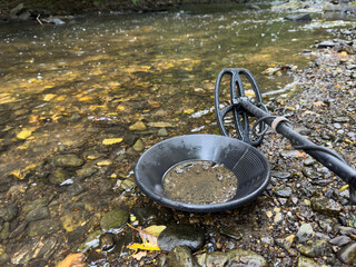 Searching for gold on a river with a gold pan and a metal detector 