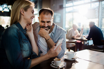 Happy couple enjoying coffee and looking at smartphone in cafe