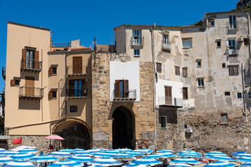 The typical houses of Cefalù seen from the sandy beach, with colorful facades, stone walls, and balconies.