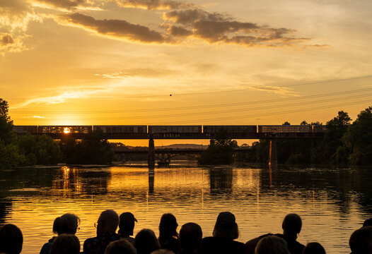 Empty freight train over the railroad bridge watched by boat tour in golden light in Austin Texas with bridges behind
