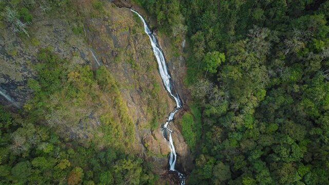 Drone view of long waterfall cascading down rocky terrain in lush forest of Costa Rica