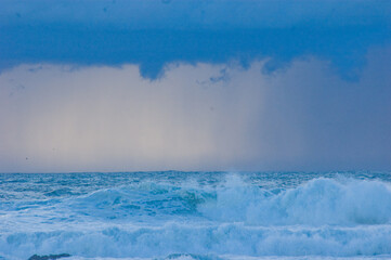 Obraz premium Waves crashing in the ocean under a cloudy sky.