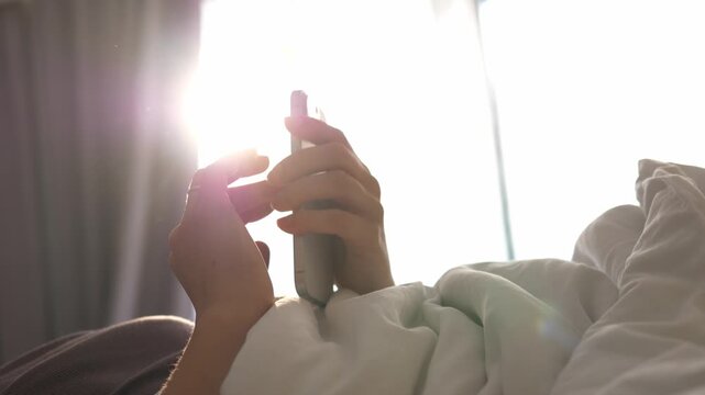 Close-up of a man's hands lying in bed and checking chats on his smartphone, browsing through mail and reading the news. Smartphone addiction