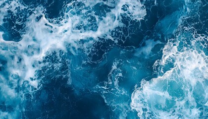 Fototapeta premium This top-down view captures the dynamic movement of deep blue ocean water, where white foam patterns swirl and dissipate across the surface.