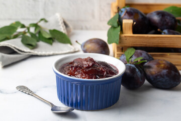 Homemade damson plum jam in blue ceramic bowl and berries on white wooden background.