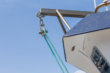 Boat pulley system with green rope hanging from metal frame against blue sky